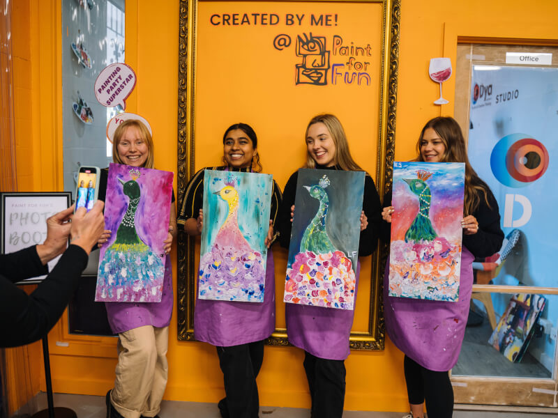 A group of women holding up painted canvases at an art class.